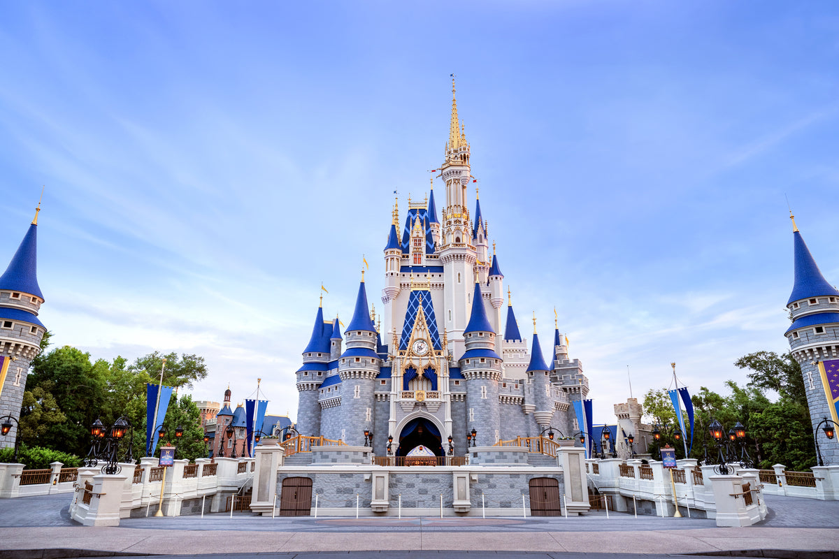 A majestic fairytale castle with blue and gold turrets under a clear blue sky, framed by towers on both sides.